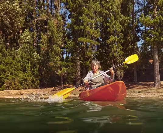 Man and woman kayaking near lake shore with forest trees in the background