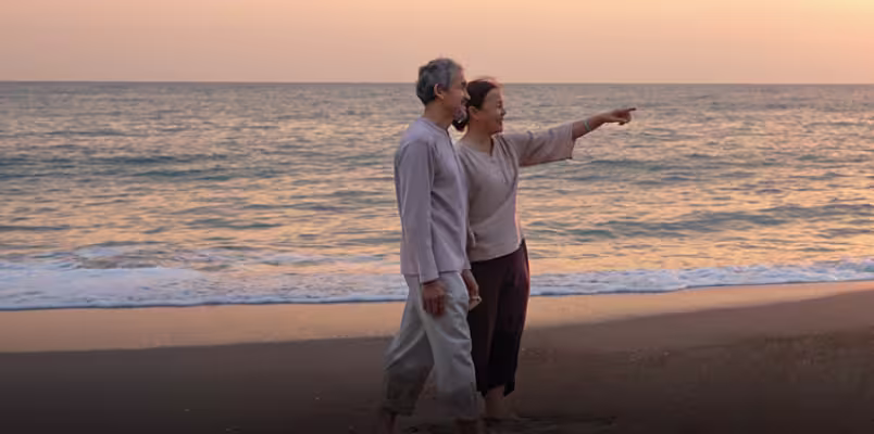 A couple walking on the beach at sunset pointing to something out of frame